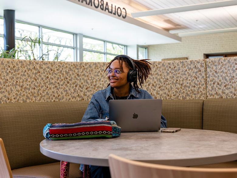 微笑的女学生坐在图书馆的桌子上，用Mac笔记本电脑.